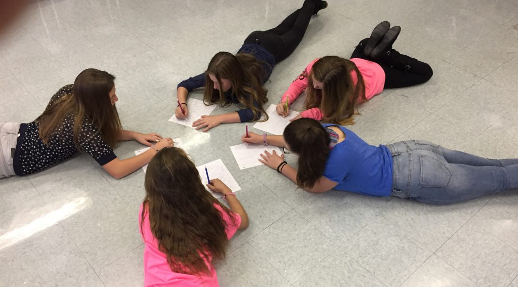 Five female students laying on the floor writing on pieces of paper